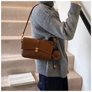 Detail of dark brown shoulder bag with suede texture, gold buckle, and plush charm