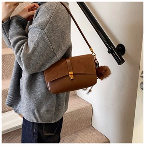 Detail of brown leather and suede shoulder bag with gold hardware and plush charm