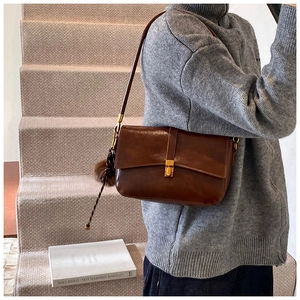 Brown faux leather crossbody bag with gold buckle and pompom charm on a model