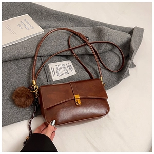 Detail of a brown leather shoulder bag with V-flap, gold buckle, and plush pompom charm