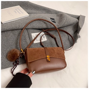 Detail of brown shoulder bag with suede拼接, gold metal buckle and plush ball charm