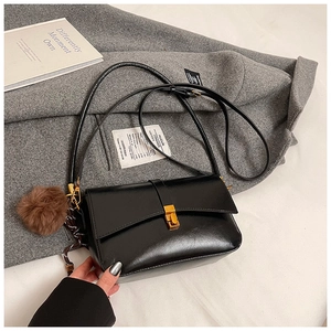 Detail of black leather crossbody bag with gold buckle and brown fur ball charm accessory