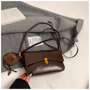 Detail of dark brown vintage leather shoulder bag with gold metal buckle and fur pompom