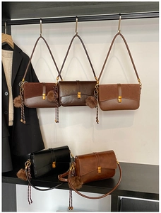 Detail of minimalist leather shoulder bag with a gold twist lock and a plush ball charm