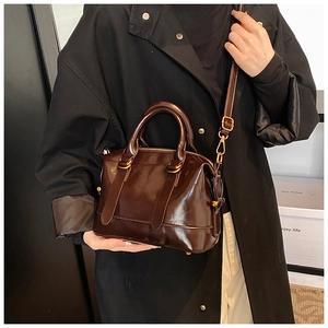 Dettaglio della borsa Boston in pelle marrone scuro lucida con manici tondi e fibbie oro