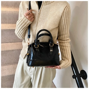 Dettaglio borsa Boston nera lucida con hardware dorato portata da una modella