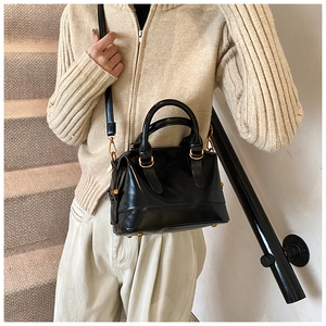 Dettaglio di una borsa a secchiello in pelle nera con finiture dorate indossata da modella