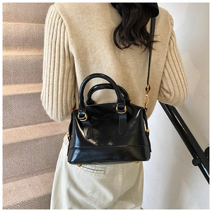 Dettaglio di una mini borsa Boston nera lucida con finiture dorate indossata dal modello