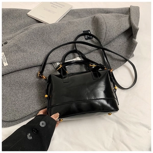 Dettaglio borsa Boston nera lucida su cappotto di lana con finiture dorate
