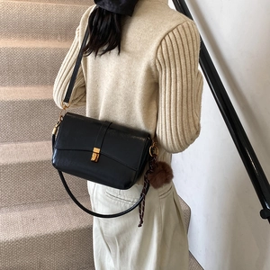 Minimalist black leather crossbody bag with gold buckle and fuzzy brown charm
