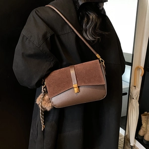 Brown suede leather underarm bag with gold buckle and pompom on black coat model