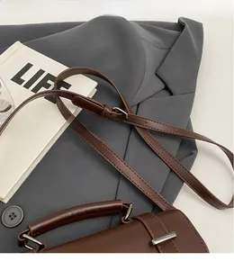 Detail of adjustable strap and silver hardware on dark brown leather crossbody bag
