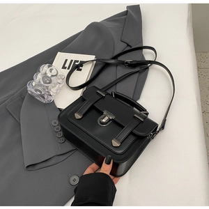 Detail of black satchel bag with silver metal buckles on a gray blazer background