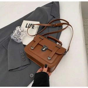 Close-up of vintage brown leather handbag with metallic push-lock on grey blazer background