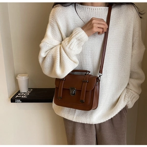 Detail of vintage brown crossbody bag with metal buckles on a knit sweater outfit
