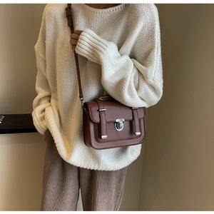 Close-up of vintage brown crossbody satchel with silver buckle on oversized white sweater