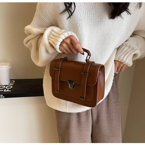 Caramel brown vintage satchel bag with metallic buckle shown with a white knit sweater