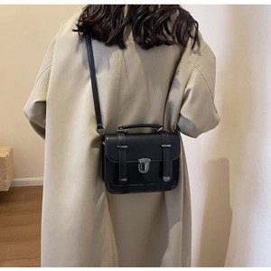 Detailed back view of a woman wearing a vintage black leather crossbody box bag over a beige coat
