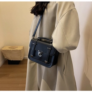 Detail view of a vintage black crossbody bag worn over a beige trench coat for women