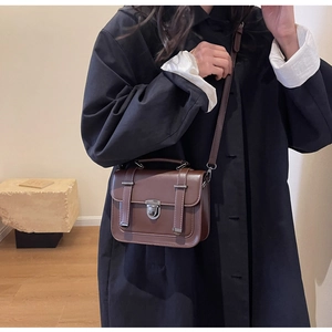 Close-up of a vintage brown leather crossbody bag styled with a classic black trench coat
