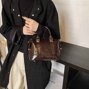 Borsa a mano Boston marrone scuro lucido con dettagli dorati in un contesto professionale