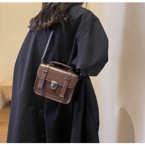 Detail of vintage dark brown crossbody bag with silver buckle and top handle on black coat