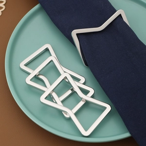 Close-up of geometric silver metal napkin rings on dark blue cloth and green plate