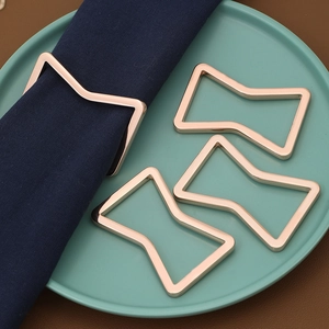 Detail of rose gold geometric bowtie napkin rings set on navy fabric over green plate