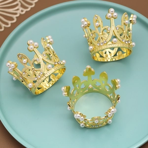 Drei goldene Serviettenringe in Kronenform mit Perlen und Strass auf einem Tablett