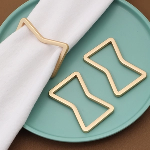 Close-up of matte gold geometric hourglass napkin rings on white cloth and ceramic plate