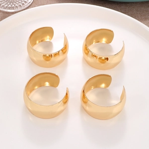 Set of four polished gold wide C-shaped napkin rings on a white plate for elegant dining decoration