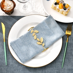 Golden leaf napkin ring made of zinc alloy on a blue linen napkin with white plate