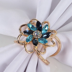 Golden flower napkin ring featuring blue crystals on elegant white fabric