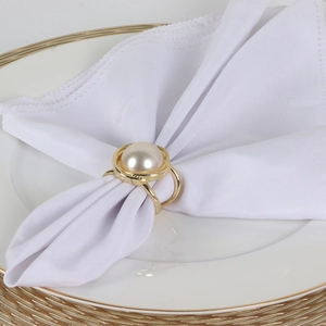 Elegant gold pearl napkin ring on a white linen napkin and ceramic plate for table decor
