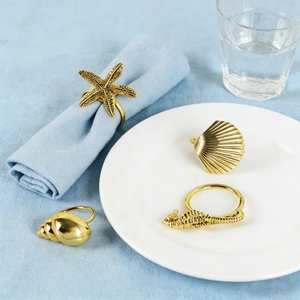 Macro detail of gold-plated ocean-themed napkin rings showing starfish and seahorse textures