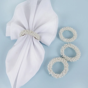 Set of four white pearl beaded napkin rings displayed on a light blue background