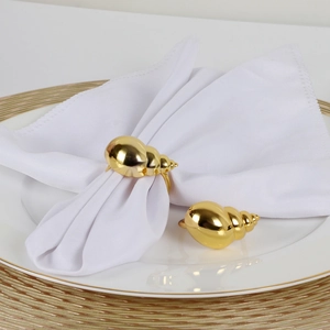 Detail of golden conch shell napkin ring on white cloth over elegant dinnerware