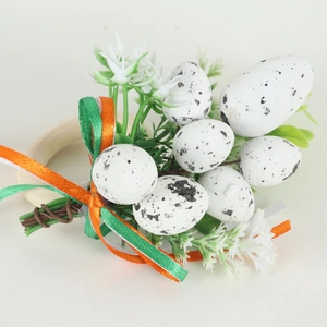 Detail of wooden Easter napkin ring with speckled eggs, green leaves, and ribbons