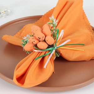 Detail of speckled Easter egg napkin ring with white flowers and green leaves on an orange cloth