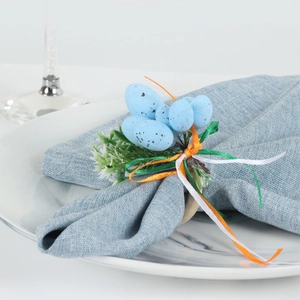 Detail of speckled Easter egg napkin ring with green foliage on a blue linen napkin