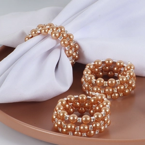 Détail de ronds de serviette en perles champagne et strass sur nappe blanche