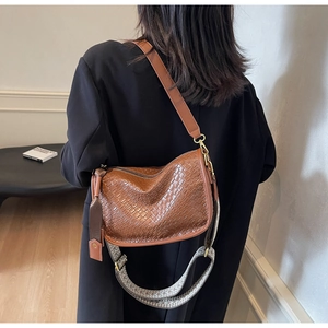 Détail d'un sac bandoulière marron tressé avec deux sangles porté avec un blazer noir