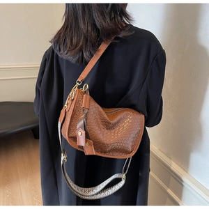 Détail d'un sac à bandoulière tressé marron avec une sangle à motif et des finitions dorées