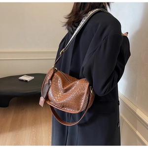 Détail d'un sac bandoulière marron tressé avec sangle jacquard porté par un mannequin chic