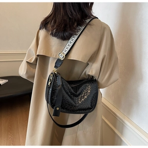 Détail du sac croissant tressé noir avec bandoulière géométrique sur un trench beige