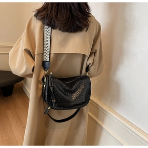 Détail d'un sac bandoulière tissé noir avec deux sangles sur un manteau beige