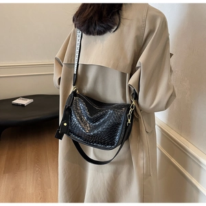 Détail d'un sac à bandoulière noir texture croco avec large sangle à motifs sur un trench