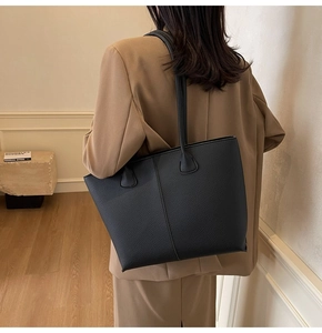 Detail of black pebbled leather tote bag worn by model showing large capacity design