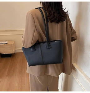 Rear view of a black lychee texture tote bag carried by a model in a camel blazer