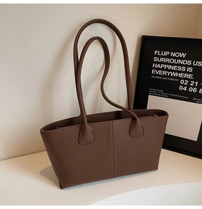 Detail of dark brown lychee grain leather tote bag with slim straps on a minimalist desk